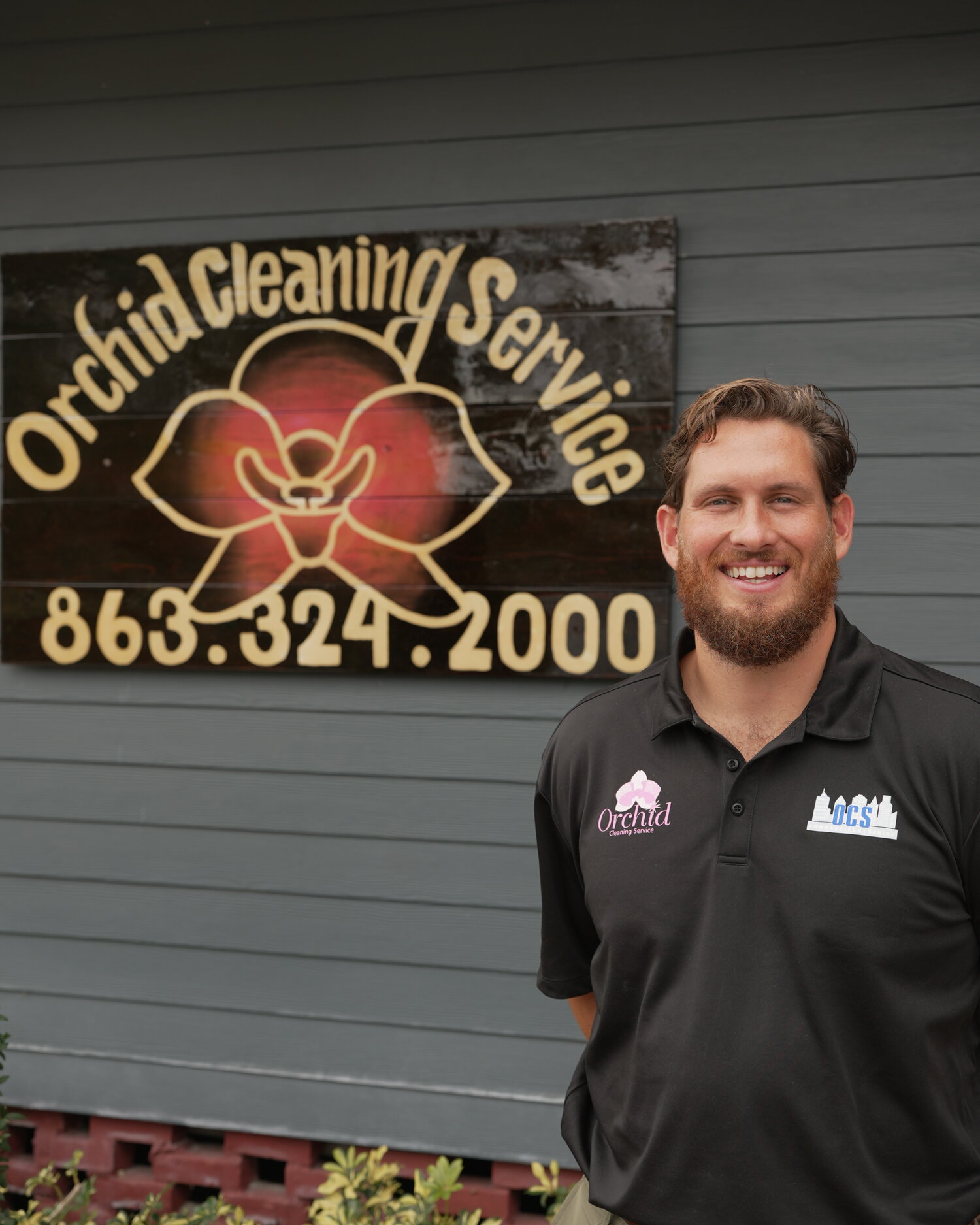 Joey Maher, owner of Orchid Cleaning Service, smiling in front of the hand-carved Orchid Cleaning sign