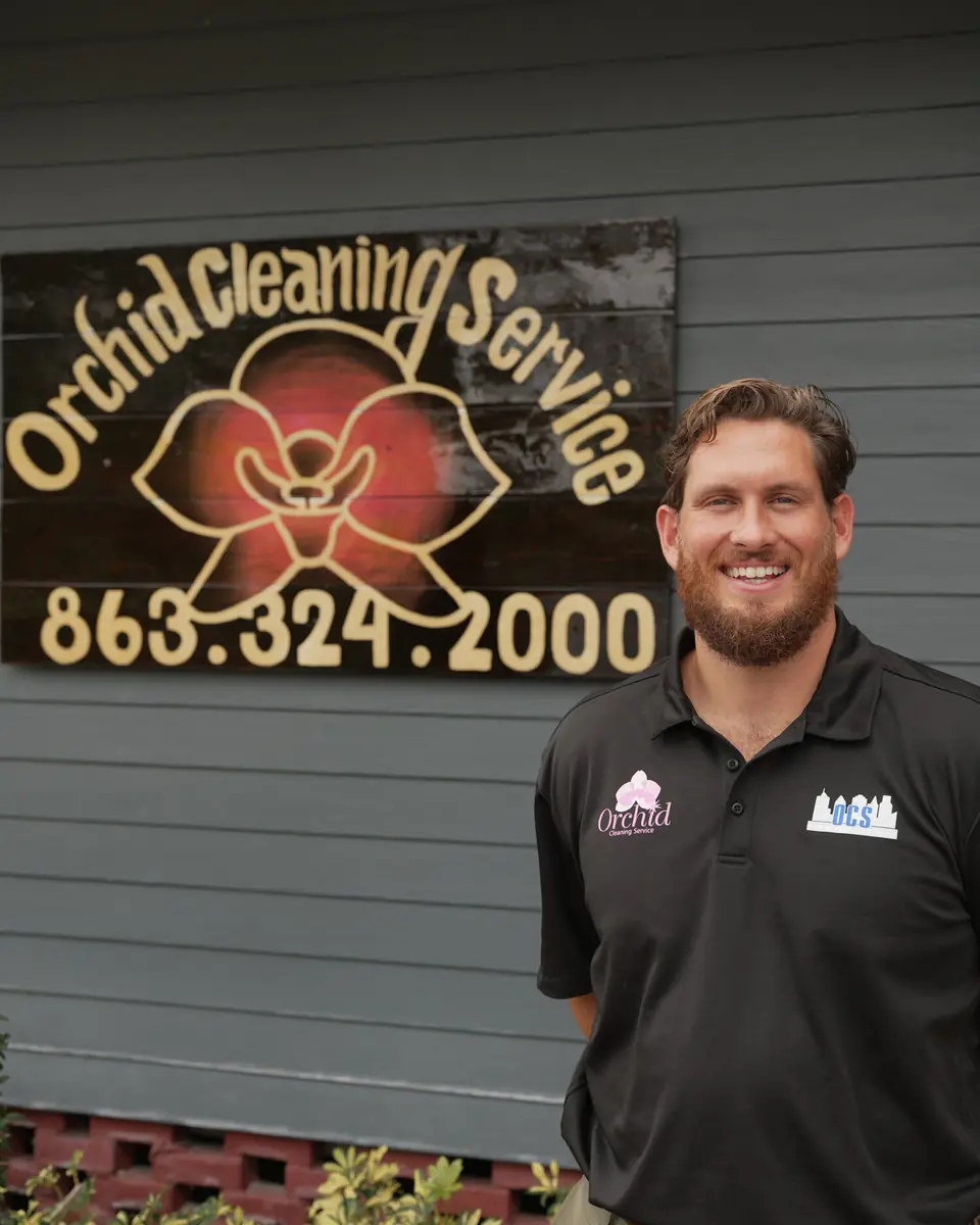 Joey Maher, owner of Orchid Cleaning Service, smiling in front of the hand-carved Orchid Cleaning sign